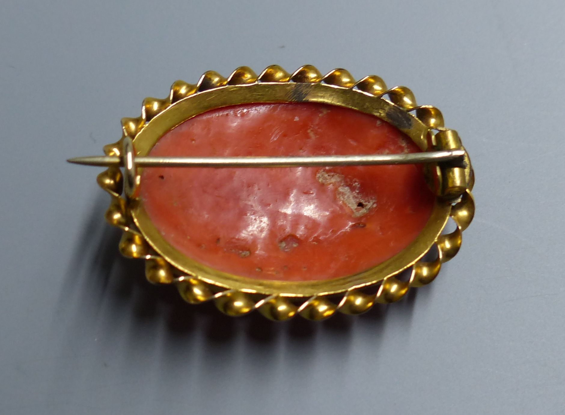 An antique yellow metal mounted oval coral set brooch, carved with a basket of flowers and fruit, 33mm, gross 6.4 grams.